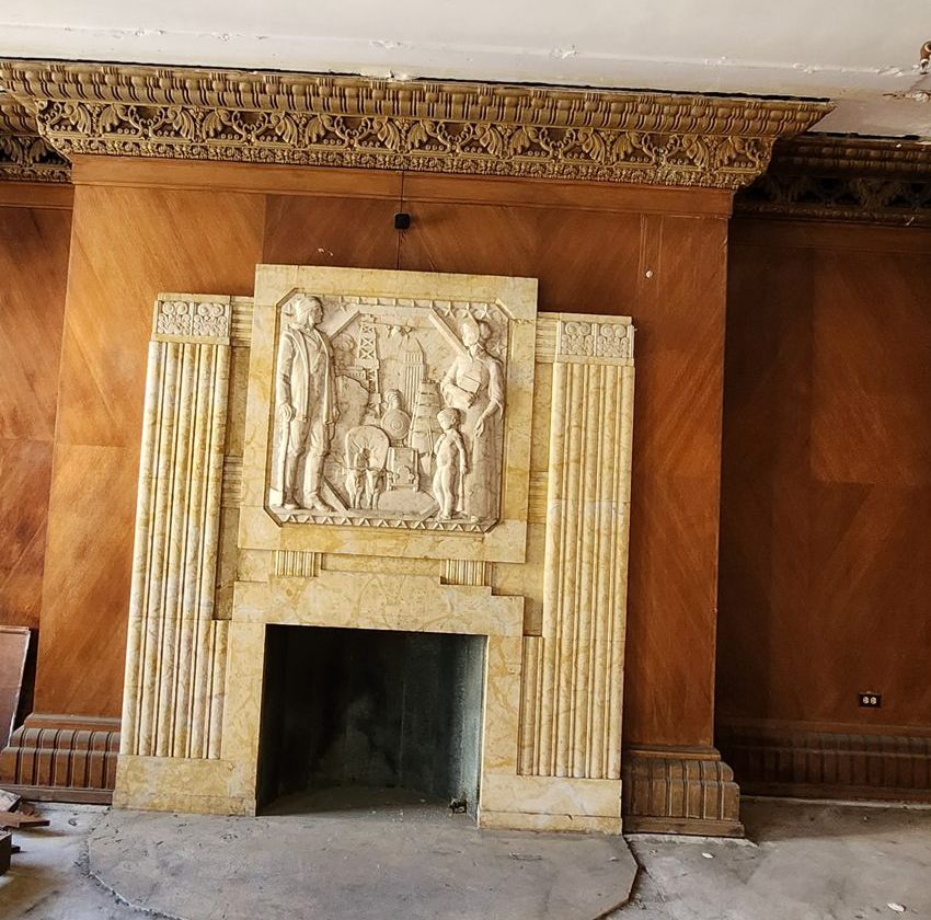 A carved stone fireplace with a relief panel set in wood paneling